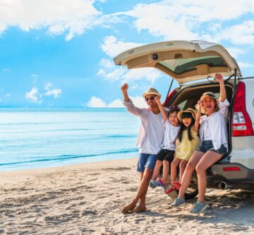 young family sitting in the back of a white SUV on the beach