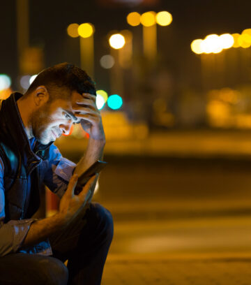 pensive young man sitting by car at night reading message