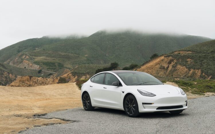 White Tesla Model 3 in the outback showing mountains and dirt road
