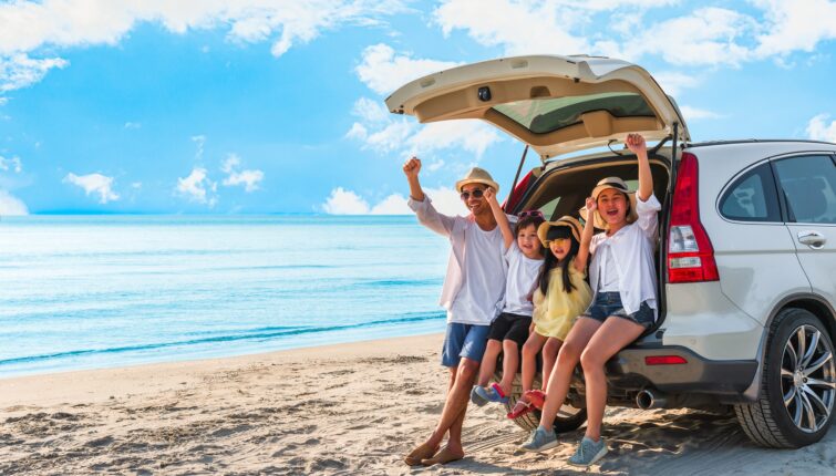 young family sitting in the back of a white SUV on the beach