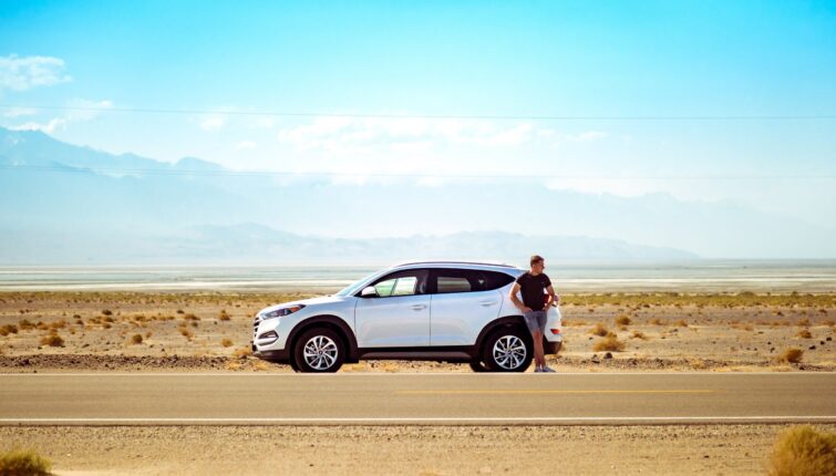 man standing outside white SUV on an open desert road