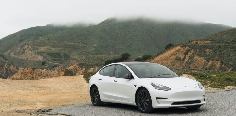 White Tesla Model 3 in the outback showing mountains and dirt road