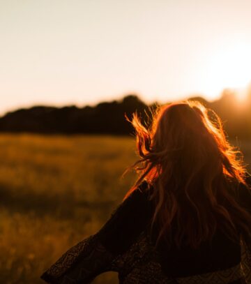 carefree woman standing in an open field during sunset