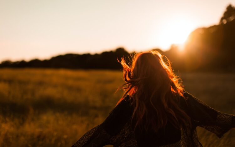 carefree woman standing in an open field during sunset