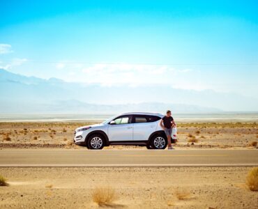 man standing outside white SUV on an open desert road
