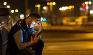 pensive young man sitting by car at night reading message