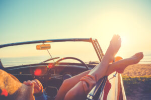 convertible car on a beach with a woman hanging her feet out of the window