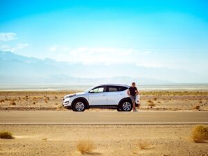 man standing outside white SUV on an open desert road