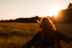 carefree woman standing in an open field during sunset