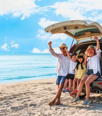 young family sitting in the back of a white SUV on the beach