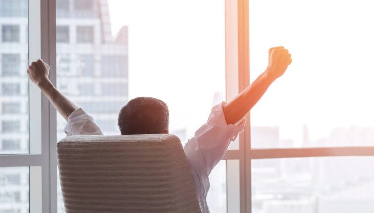 happy businessman in office raising fists looking forward to city building urban scene through glass window