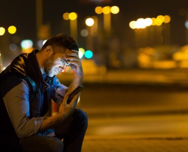 pensive young man sitting by car at night reading message