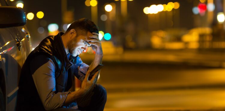 pensive young man sitting by car at night reading message