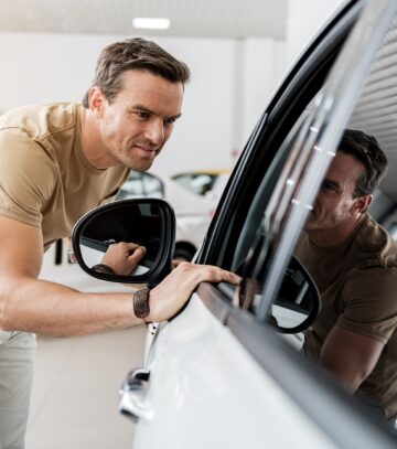 smiling man expressing concernment while looking at passenger compartment through window of a car