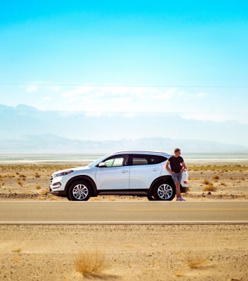 man standing outside white SUV on an open desert road