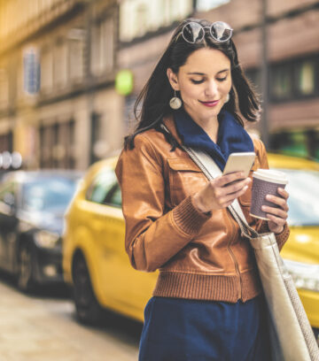 woman on phone with a coffee cup walking in the city