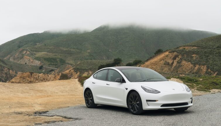 White Tesla Model 3 in the outback showing mountains and dirt road