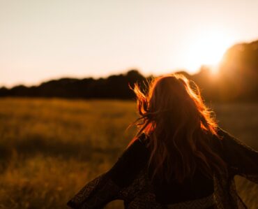 carefree woman standing in an open field during sunset