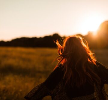 carefree woman standing in an open field during sunset