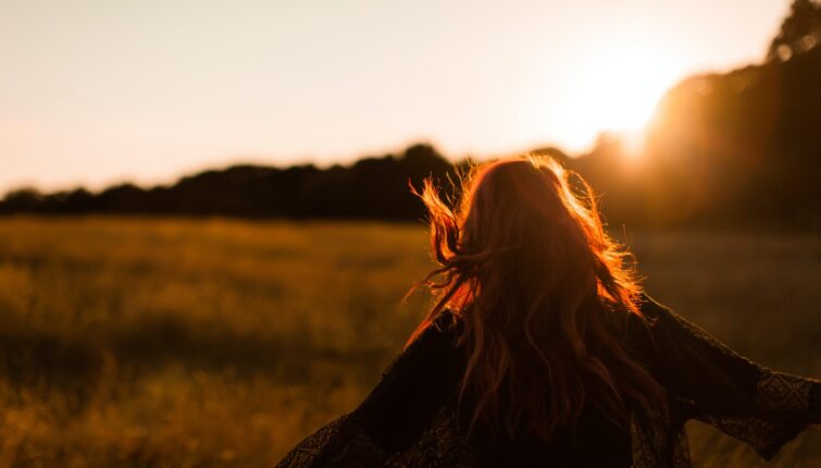 carefree woman standing in an open field during sunset